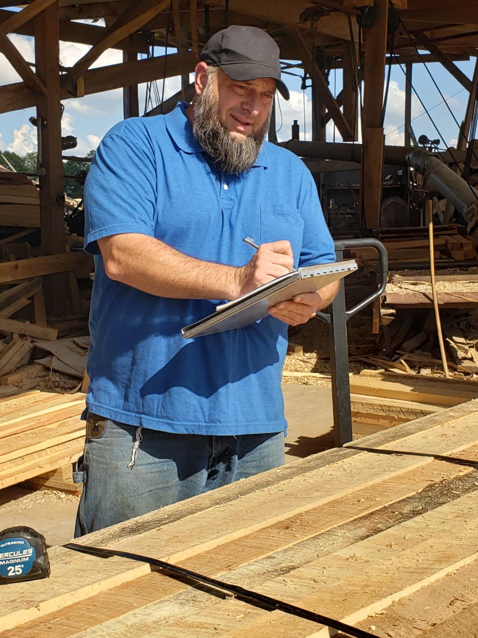 Person writing on a clipboard beside stacked lumber at a wood-products facility